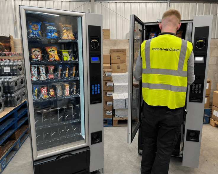 Un technicien remplit un distributeur de snacks dans l'entrepôt, une seconde machine porte ouverte à côté